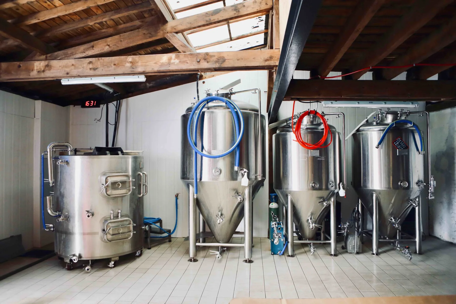 La salle de brassage : la cuve d’empâtage et trois fermenteurs inox sous la charpente en bois